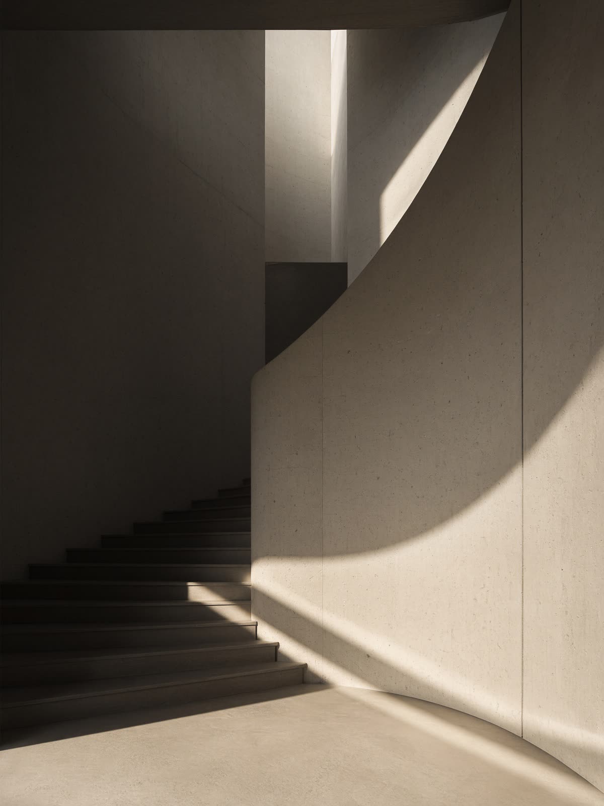 Cage d’escalier en béton, un rai de soleil sur la pierre.